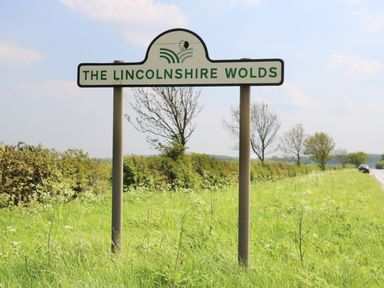 A roadside sign for The Lincolnshire Wolds with grass trees and a car on the road in the background at Heron Lodge in Mavis Enderby near Spilsby