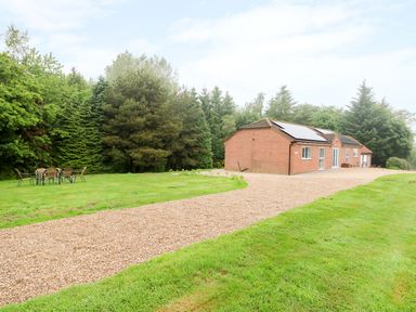 A gravel driveway leading to a brick house with solar panels next to a grassy area with outdoor chairs and a table at Heron Lodge in Mavis Enderby near Spilsby