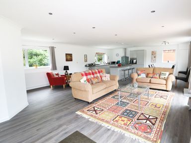 An open living room with two beige sofas a colorful rug a glass coffee table and a kitchen area at Heron Lodge in Mavis Enderby near Spilsby