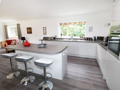 A kitchen with white cabinets, an island with three bar stools, and a red armchair at Heron Lodge in Mavis Enderby near Spilsby