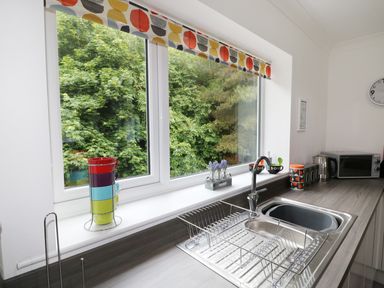 A kitchen counter with a sink drying rack colorful mugs a kettle a microwave and a window with a patterned valance at Heron Lodge in Mavis Enderby near Spilsby