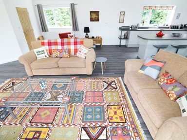 A living room with two beige sofas a colorful patterned rug and a glass coffee table at Heron Lodge in Mavis Enderby near Spilsby