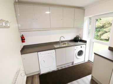 A utility room with a washer, dryer, sink, cabinets, and a door leading outside at Heron Lodge in Mavis Enderby near Spilsby
