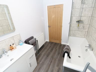 A bathroom with a sink and cabinet a towel rail a wooden door and a bathtub with a shower at Heron Lodge in Mavis Enderby near Spilsby