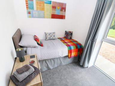 A bedroom with a single bed colorful pillows a bedside table and a large window at Heron Lodge in Mavis Enderby near Spilsby
