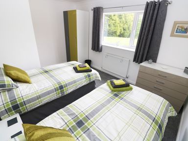 A bedroom with two single beds with plaid bedding a wardrobe a chest of drawers and a window with curtains at Heron Lodge in Mavis Enderby near Spilsby