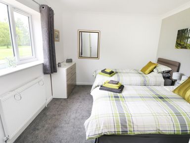 A bedroom with two single beds with plaid bedding a window a dresser with a mirror and gray curtains at Heron Lodge in Mavis Enderby near Spilsby
