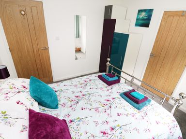 A bedroom with floral bedding two wooden doors a tall wardrobe and a wall mirror at Heron Lodge in Mavis Enderby near Spilsby