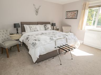 A bedroom with a double bed bedside tables chairs a window and a wall decoration at Manor House in Warkworth