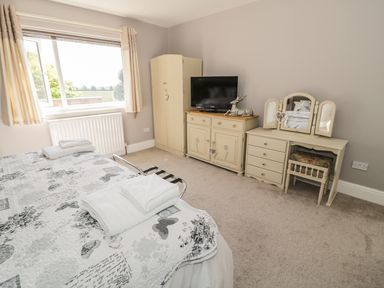 A bedroom with a bed covered with a patterned quilt and folded towels a dresser with a television a wardrobe and a dressing table with a chair at Manor House in Warkworth