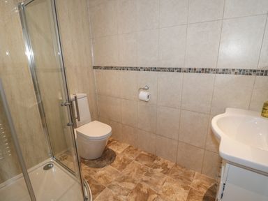 A bathroom with a glass shower enclosure a toilet a sink and tiled walls and floor at Manor House in Warkworth
