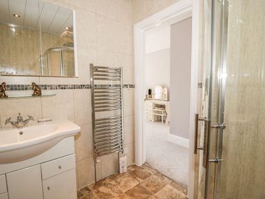 A bathroom with a sink cabinet mirror towel radiator and a shower visible next to an open door to a bedroom with a dresser at Manor House in Warkworth