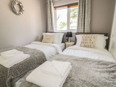 A bedroom with two single beds a window between the beds and a small round bedside table with a lamp a wreath on the wall at Manor House in Warkworth