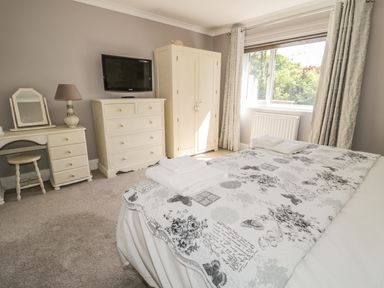 A bedroom with a bed covered in patterned bedding towels on bed a dresser wardrobe vanity desk and window at Manor House in Warkworth