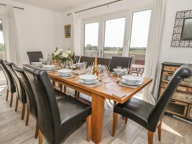 A dining room with a wooden table set for eight with black chairs and glass doors leading outside at Manor House in Warkworth