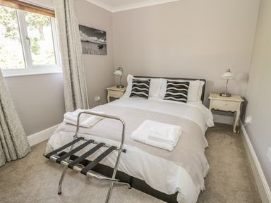 A bedroom with a double bed two bedside tables with lamps a luggage rack and a window at Manor House in Warkworth