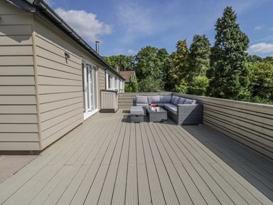 A wooden deck with outdoor sofa seating and table surrounded by trees at Manor House in Warkworth