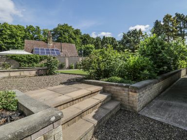 An outdoor garden area with stone steps green plants a gravel path and a house with solar panels in the background at Manor House in Warkworth