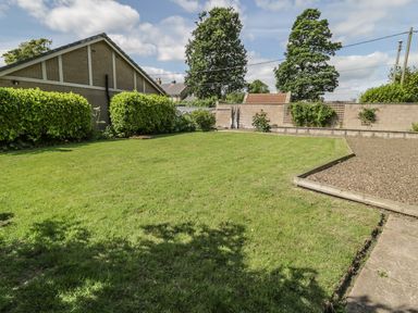 A garden with a lawn bordered by hedges and a gravel area next to a paved path at Manor House in Warkworth
