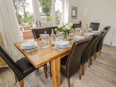 A wooden dining table set with plates glasses cutlery and a flower arrangement surrounded by brown leather chairs at Manor House in Warkworth