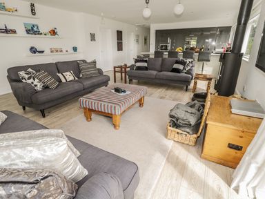A living room with three gray sofas a striped ottoman a wooden chest and a black stove at Manor House in Warkworth