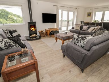 A living room with gray sofas a wooden side table a striped ottoman a wood-burning stove and a wall-mounted tv at Manor House in Warkworth