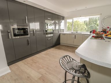 A modern kitchen with gray and beige cabinets a built in microwave and oven a large window and a metal stool at Manor House in Warkworth