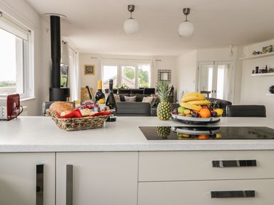 A kitchen island with a basket of bread and bottles and a fruit bowl with pineapples and bananas in a living room at Manor House in Warkworth