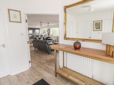 A hallway with a wooden console table and large mirror looking into a living room with gray sofas at Manor House in Warkworth