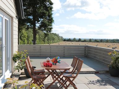 An outdoor patio with a wooden table and four chairs with fields and trees in the background at Manor House in Warkworth