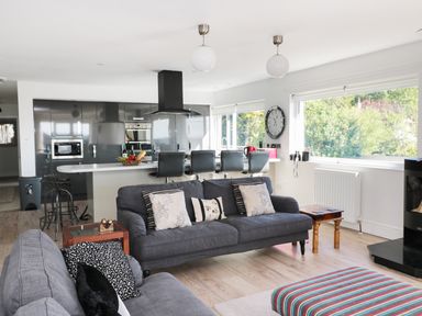 A living room and kitchen area with sofas, bar stools, a clock on the wall, and large windows at Manor House in Warkworth