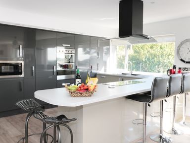 A modern kitchen with a white island countertop with bar stools and a basket of fruits and wine bottles at Manor House in Warkworth