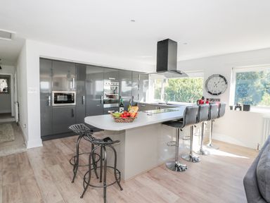 A modern kitchen with grey cabinets an island with bar stools and large windows at Manor House in Warkworth