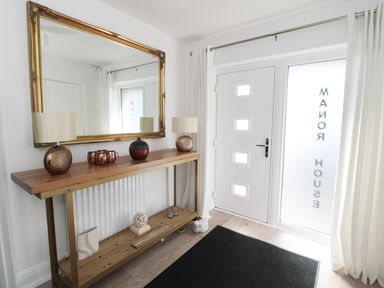 An entryway with a wooden console table holding lamps and decorative items a large mirror and a white door with frosted glass at Manor House in Warkworth