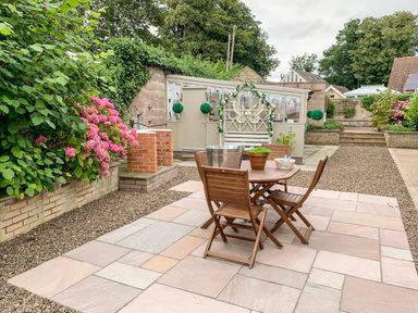An outdoor patio area with a wooden table and chairs surrounded by potted plants and flowers at Manor House in Warkworth