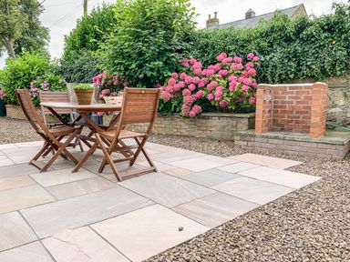 An outdoor patio area with a wooden table and chairs with potted plants and brick barbecue at Manor House in Warkworth