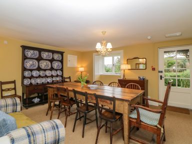 A dining room with a wooden table and mixed chairs including armchairs a cabinet with blue and white plates a sideboard with a mirror and lamps at Crannacombe Farmhouse Loddiswell