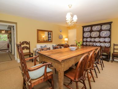 A dining room with a wooden table surrounded by chairs and a cupboard displaying blue and white plates at Crannacombe Farmhouse in Loddiswell