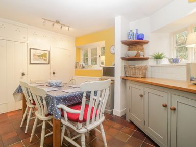 A kitchen with a dining table and chairs and cabinetry with shelves at Crannacombe Farmhouse in Loddiswell
