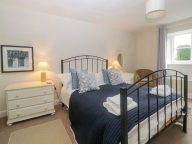 A bedroom with a black metal bed frame blue bedding white folded towels two white dressers with lamps a wicker chair and a window at Crannacombe Farmhouse Loddiswell