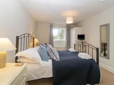 A bedroom with a bed with blue and white pillows bedside table with lamp window with curtains wardrobe television and a wall mirror at Crannacombe Farmhouse in Loddiswell