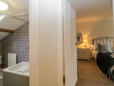 A bathroom with a bathtub and patterned tile wall next to a bedroom with a bed and bedside table lamp at Crannacombe Farmhouse in Loddiswell