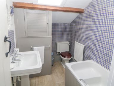 A bathroom with a sink a toilet a bathtub patterned blue and white walls and wooden floor at Crannacombe Farmhouse in Loddiswell