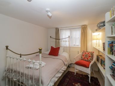 A bedroom with a single bed rolled towels a wicker chair with cushions a bookshelf and a window with curtains at Crannacombe Farmhouse in Loddiswell