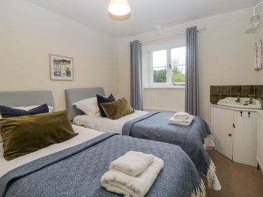 A bedroom with two single beds with blue blankets and folded towels by a window at Crannacombe Farmhouse in Loddiswell