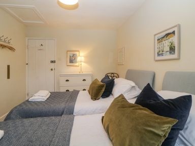 A bedroom with two single beds with pillows and blankets a chest of drawers with a lamp and framed pictures on the walls at Crannacombe Farmhouse in Loddiswell