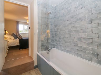 A bathroom with a bathtub and tiled wall next to a bedroom with a bed and window at Crannacombe Farmhouse in Loddiswell