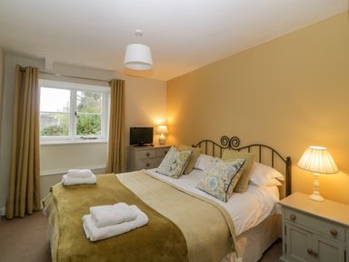 A bedroom with a double bed bedside tables lamps a dresser with a small tv and windows with curtains at Crannacombe Farmhouse in Loddiswell