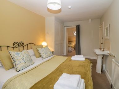 A bedroom with a bed arranged with pillows towels and a blanket a bedside lamp a sink and an open doorway showing another bedroom at Crannacombe Farmhouse in Loddiswell
