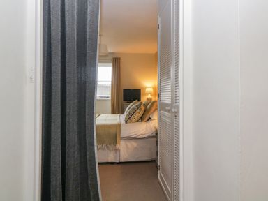 A bedroom seen through a doorway with a bed pillow and blanket a television on a stand and window with curtains at Crannacombe Farmhouse in Loddiswell